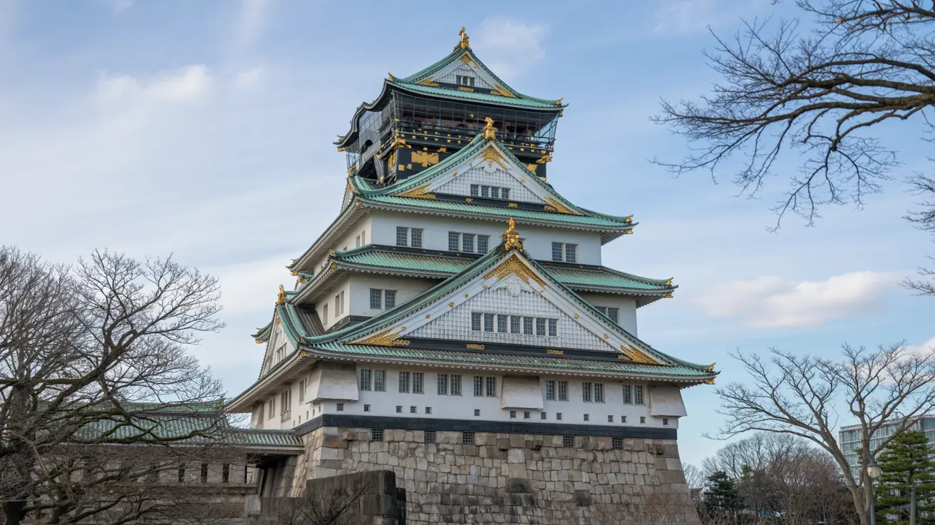 Pemandangan Istana Osaka yang ikonik dengan struktur bertingkat beratap hijau kebiruan, dinding putih elegan, aksen emas berkilau, dan dasar batu kokoh di bawah langit biru cerah dengan pepohonan gundul musim dingin yang samar.